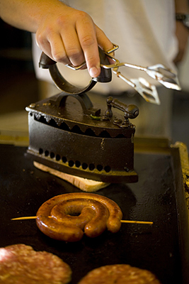 Hungary - Pecs - A chef irons a piece of fried bread on a griddle with a sausage at a food stall