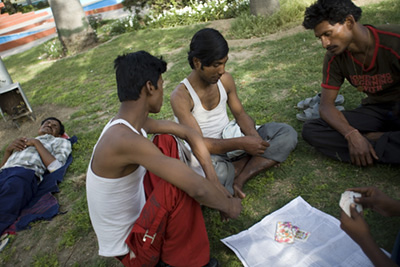 India - New Delhi - Men play cards on a traffic island in New Delhi, India whilst one of their friends sleep. The traffic islands in the centre of the city often have manicured lawns and are well cared for. Many people sleep here at night but in the daytime they are used as small parks by workers