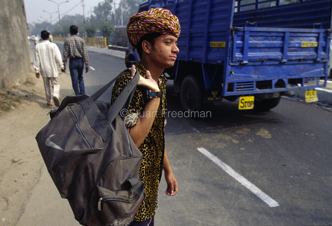 India - New Delhi - A boy on his way to perform his magic act at a wedding waits for a lift by the side of the road